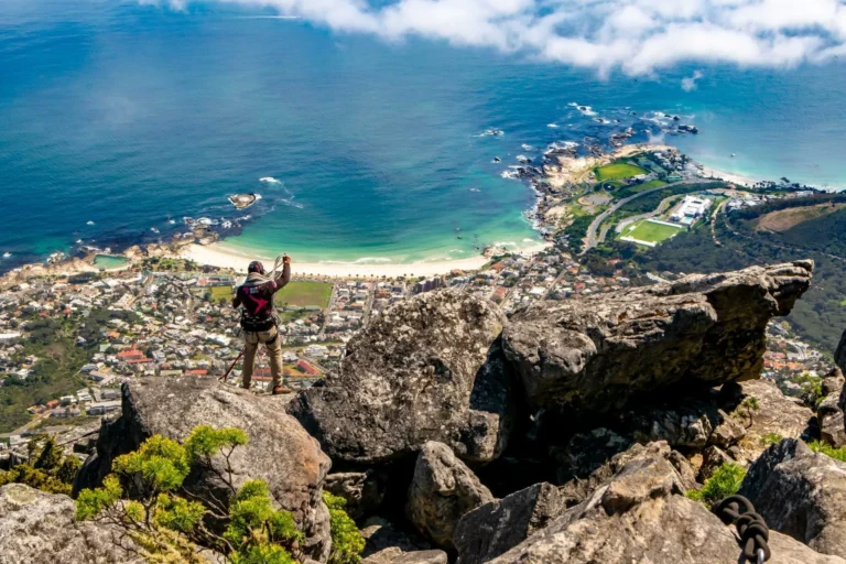 man with climbing equipment standing on table mountain overlooking a beach, be sure to bring the right gear for your south africa packing list