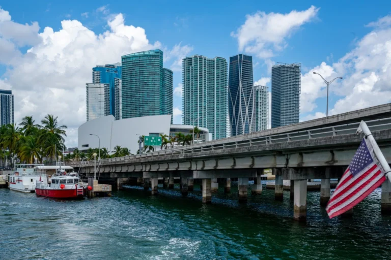 Photo of Miami skyline with a US flag in the right corner and a causeway built over the water. Miami is easily one of the best weekend getaways in the USA!