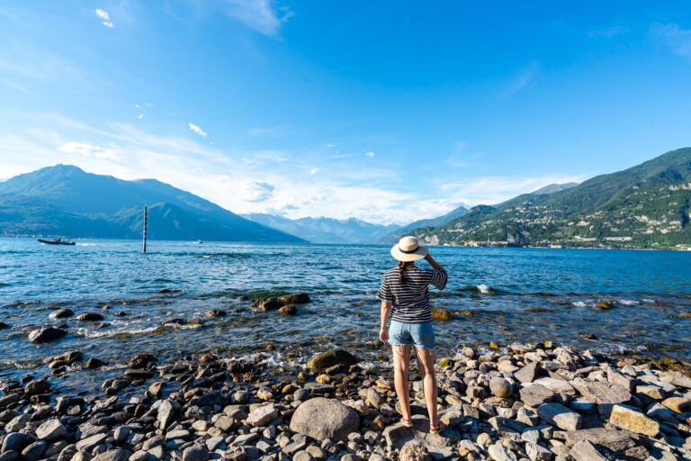 kate storm in shorts and a sunhat overlooking lake como from a rocky beach